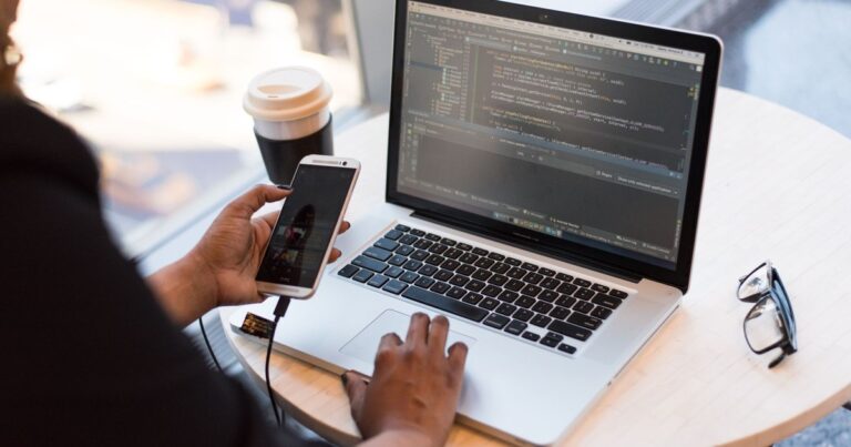 Developer writing web app code on a laptop while checking a phone